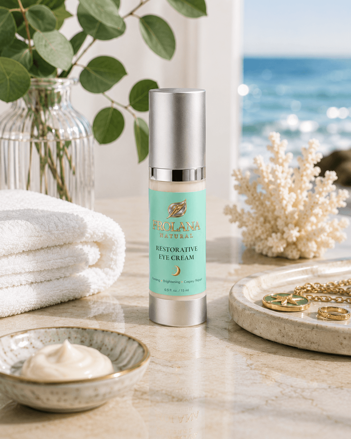 Frolana Natural Restorative Eye Cream for mature skin, displayed on a marble surface in a spa-like coastal setting with folded white towels, a bowl of cream, coral decor, and an ocean view.