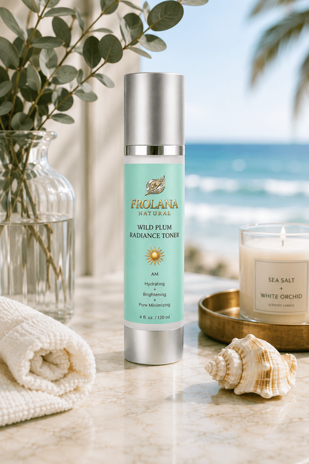 A bottle of Frolana Natural Wild Plum Radiance Toner stands on a marble surface with a beach and ocean blurred in the background. The scene includes a glass vase with eucalyptus, a rolled cream towel, a seashell, and a candle labeled Sea Salt + White Orchid.